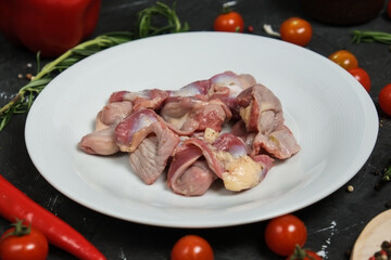 Chicken ventricles in a in a white plate, fresh rosemary, fresh cherry tomatoes, fresh chili peppers, garlic, lime and sea salt on a black background.