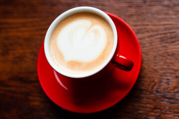 Hot coffee with latte art in a white cup with saucers on a wooden table. Cappuccino with foam. Cup of coffee on a wooden table. Top view. Place for text. Cappuccino with latte.