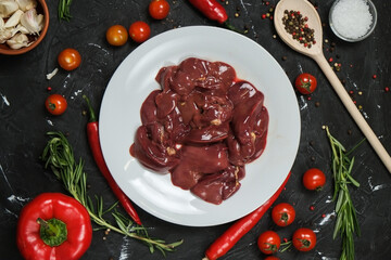 Chicken ventricles in a in a white plate, fresh rosemary, fresh cherry tomatoes, fresh chili peppers, garlic, lime and sea salt on a black background.