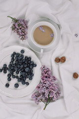 Obraz na płótnie Canvas Coffee, blueberries, lilac flowers on white linen. White crockery.