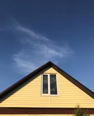 a sloping roof with a window in the attic against the blue sky