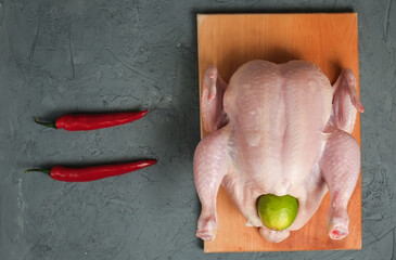 Raw whole chicken with chili peppers and lime on a wooden board on a light background