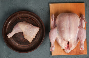 raw chicken leg in a plate and a whole chicken on a blackboard on a light background