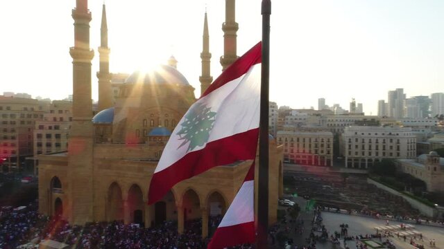 Beirut, Lebanon 2019 : sunset slow motion drone shot around Lebanese flag in martyrs square with church and mosque and sun flaring in the background during the Lebanese revolution 