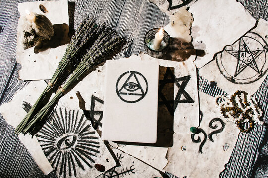 White magic book laying on the table with old manuscripts with occult symbols, candles, lavender. Concept of fortune telling, ritual, altar, spiritism, secret knowledge
