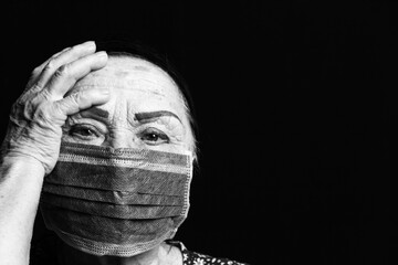 Close up black and white portrait of an elderly woman in medical mask on a black background. Old people in risk zone because of virus epidemy, COVID-2019 pandemic