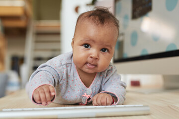 Front view portrait of cute African-American baby looking at camera while crawling on desk at home...