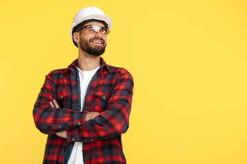 Handsome bearded engineer or constructor man in plai shirt standing over yellow background. Looking away.