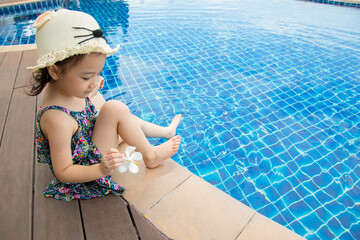 Selective focus and above shot with copy space of adorable 4-year-old asian girl sitting beside the pool with blue and clear water with fun and happiness during the summer vacation with the family.