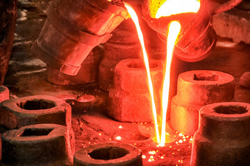 The metal workers is pouring molten metal to molds. Sand casting allows for smaller batches than permanent mold casting and at a very reasonable cost.