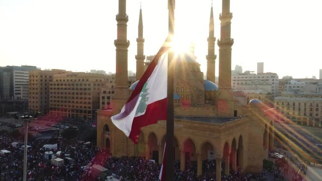 Beirut, Lebanon 2019 : sunset slow motion drone shot around Lebanese flag in martyrs square with church and mosque and sun flaring in the background during the Lebanese revolution 