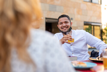 the new normality after the coronavirus epidemic, focus on the young man drinking a beer, wearing the protective mask under his chin and keeping social distancing. Happy an positive  concept