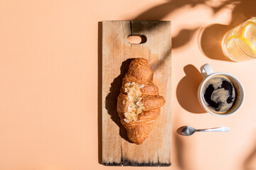 top view of coffee, water and croissant on wooden board for breakfast on beige table