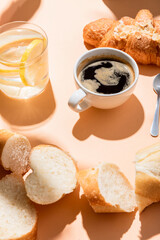 cup of coffee, croissant, water and baguette for breakfast on beige table