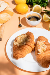 croissants, baguette, lemons and cup of coffee for breakfast on beige table