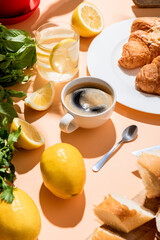 coffee, croissants, water with lemon for breakfast on beige table