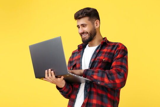 Smiling Bearded Hipster Young Man In Plaid Shirt Using Notebook Or Computer Over Yellow Background.