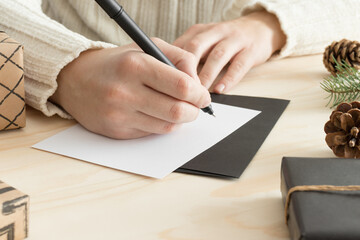 Woman writing a christmas card on a wooden table with christmas decoration.