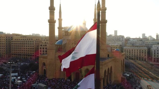 Beirut, Lebanon 2019 : sunset drone shot ped down on Lebanese flag in martyrs square with church and mosque and sun flaring in the background during the Lebanese revolution 
