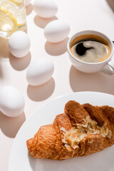 eggs, croissant, coffee and water with lemon for breakfast on grey table with shadows