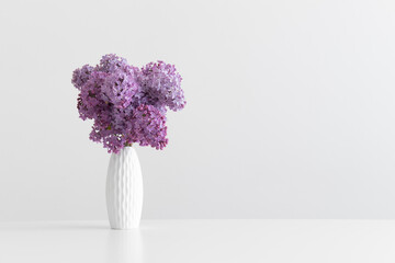 Bouquet of lilac flowers in a vase on a white table with blank copy space.
