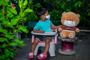 A child and his doll spend time sitting in the garden wearing face masks in on coronavirus pandemic time.