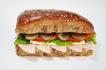 Juicy sandwich from dark flour with cucumbers, lettuce, cheese and ham on a white background