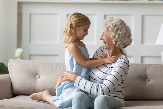 Older grandmother spend pleasant time with pretty granddaughter. Different age generations relatives people having warm relations, enjoy weekend talk seated on couch at home. Love protection concept