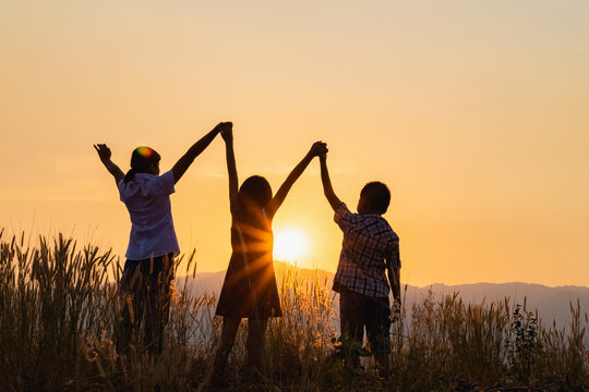 Silhouette of happy children standing with raised hands on the mountain at the sunset time.