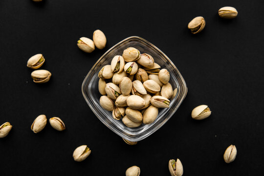 Pistachios in a small plate with scattered nuts of almonds around a plate on a black surface. Pistachio is a healthy vegetarian protein nutritious food. Natural nuts snacks.