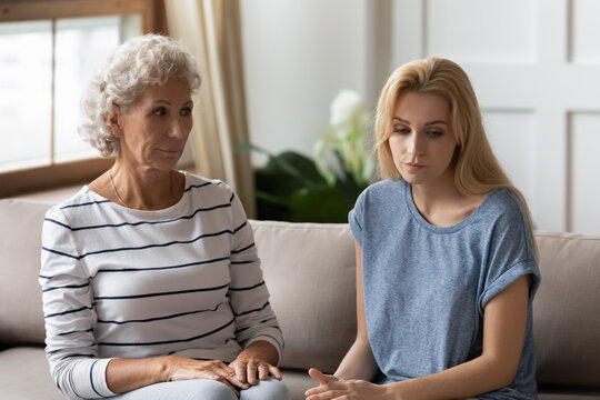 Generational Gap, Misunderstanding, Different Opinions And Multi Generational Family Conflict Concept. Elderly 50s Mom Grown Up Daughter Sit On Couch In Silence Thinking Feeling Annoyed After Dispute