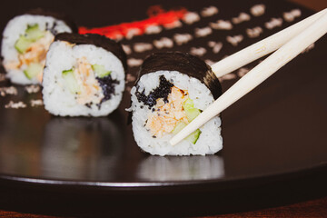 Chopsticks hold a sushi roll with salmon and fresh cucumber.