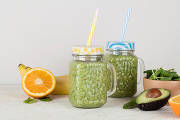 Green smoothie on gray background with avocado, spinach, banana, orange.