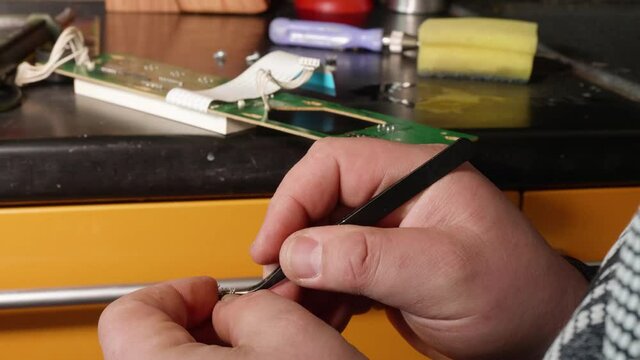 Man's hands fix microswitch of electrical card using tweezers.
