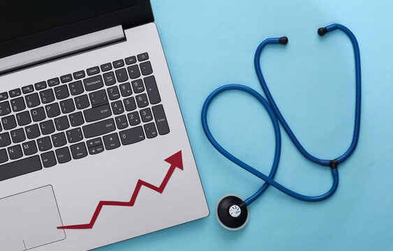 Laptop, Stethoscope with growth arrow on blue background. Top view