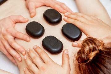 Obraz na płótnie Canvas Male four hands laying large new oval black hot stones for back massage on female back in spa salon
