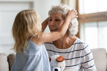 Cutie small granddaughter imagines herself like princess play with elderly grandmother puts on her...