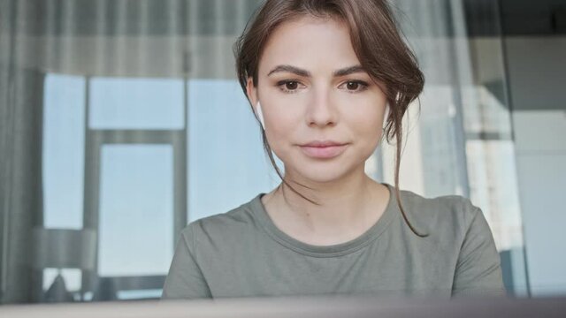 An attractive young woman with earbuds is working while using her laptop computer sitting at home