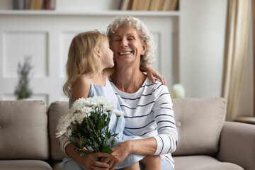Tender little granddaughter kiss on cheek old grandmother today she is birthday girl. Small kid congratulates granny with Women Day 8-march express love make surprise gave flowers as pleasant gesture