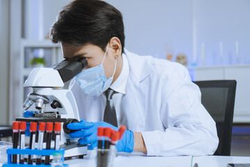 Young Asian handsome man scientist adjust focus and use Microscope to looking biochemical cell in laboratory. Doctor and scientist work in laboratory pandemic of corona virus, COVID19 concept