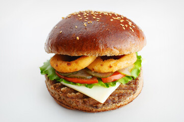 Juicy burger from dark flour with onion rings, cucumbers, lettuce, cheese on a white background