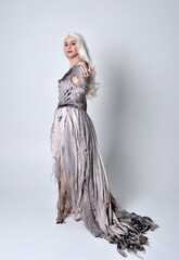 full length portrait of blonde girl wearing long torn old wedding dress.  standing pose with back to the camera on a studio background.