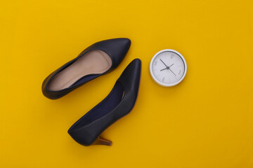Women's shoes with heels and clock on yellow background. Top view