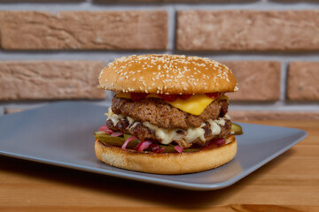 Juicy burger with onion, cucumbers, lettuce, cheese lie on a wooden table. brick background