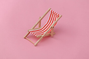 Red and white striped mini beach deck chair on pink background. Symbol of beach holidays, resort. ...