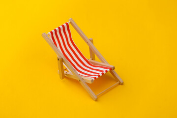 Striped mini beach deck chair on Yellow background. Symbol of beach holidays, resort.  Relax, Summer minimal concept