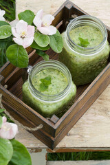 Green smoothie on old stool near flowers on nature