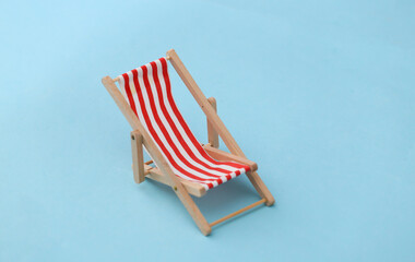 Striped mini beach deck chair on blue background. Symbol of beach holidays, resort.  Relax, Summer minimal concept