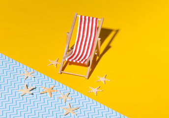 Mini beach deck chair and starfish on yellow blue background with shadow. Sunlight. Symbol of beach holidays, resort.  Relax, Summer minimal concept.