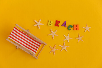 Fototapeta na wymiar Mini beach deck chair and starfish on yellow background. Word beach. Symbol of beach holidays, resort. Relax, Summer minimal concept. Top view